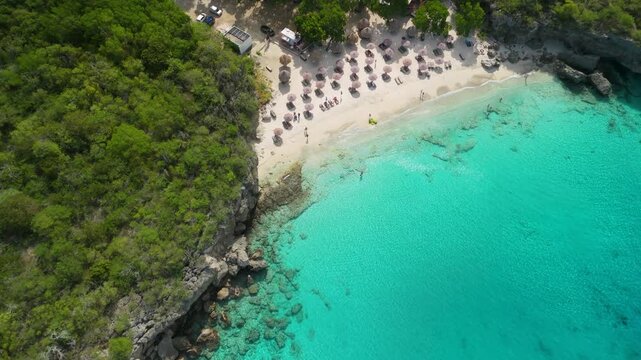 Aerial top down descent over turquoise sea with slow tilt up revealing sandy Kleine Knip Beach in Curacao