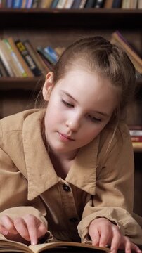 Close up of a serious little girl focused on reading a textbook. The smart kid is preparing for an exam in the library, her finger tracing the words on the page as she studies intently