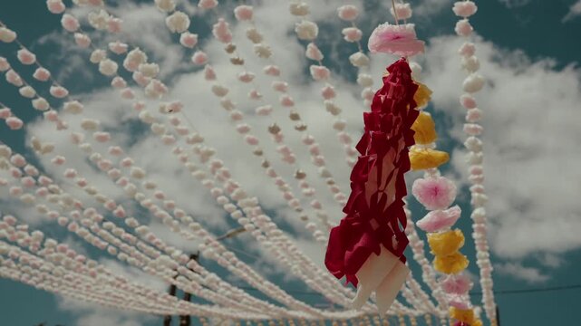 Diamond pattern red streamer hangs beside pompom flowers and beaded strings against sky at arraial festival