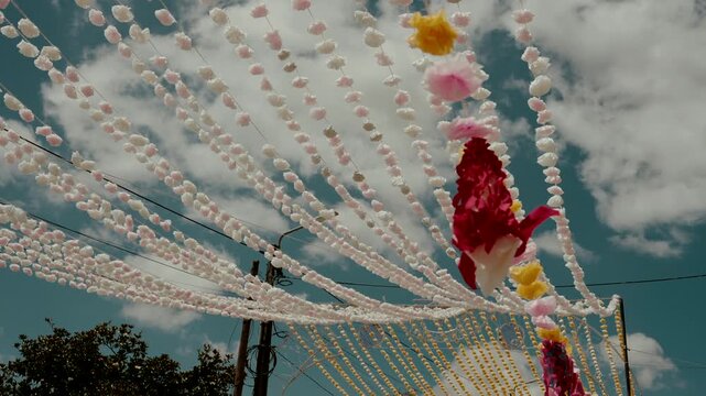 Rows of pink bead strings radiate from a knot beside red streamer over utility pole at arraial festival
