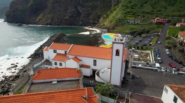 Ponta Delgada Madeira Portugal 4K Drone. Backward orbit  flight over church to ocean revealing coastal village natural pools and mountains. Scenic aerial b roll cinematic travel stock video asset