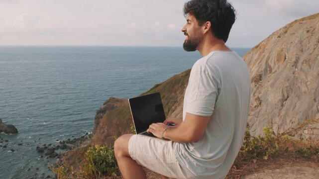 Digital nomad working remotely on a cliff overlooking the ocean