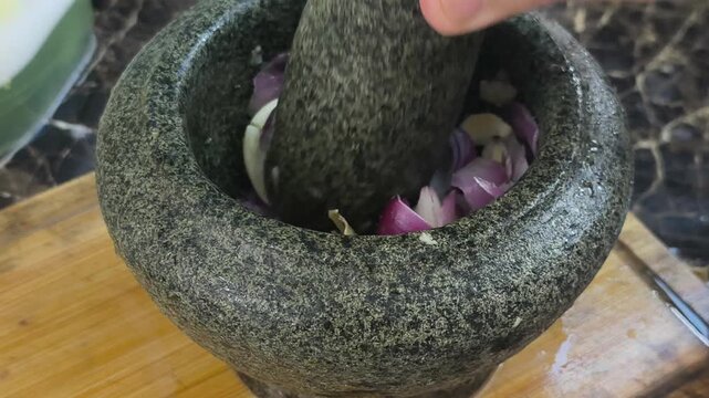Onions and anchovies are crushed together using a traditional stone mortar and pestle. This authentic method prepares flavorful ingredients for cooking. It captures a classic culinary technique.