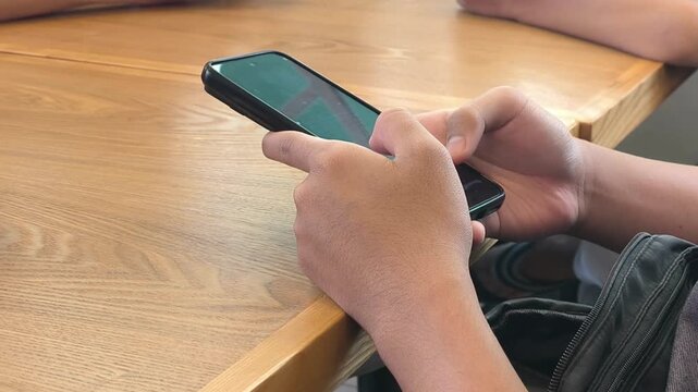 A teenager uses a smartphone while sitting at a dining table. Their finger smoothly scrolls through social media feeds. This scene highlights modern youth digital habits during downtime.