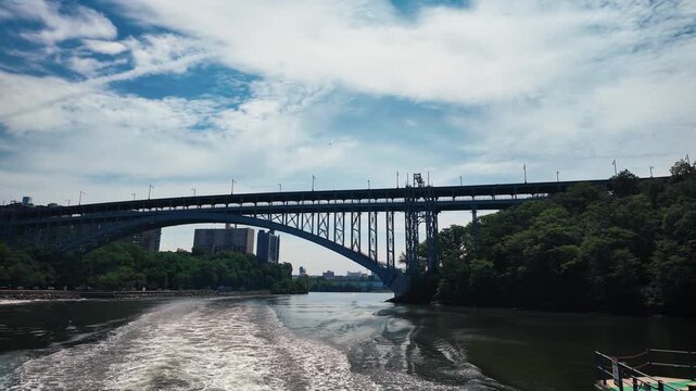 Cinematic stern view from a moving boat passing through the historic Spuyten Duyvil Railroad Swing Bridge with the Henry Hudson Bridge spanning the Harlem River in northern Manhattan, New York City.