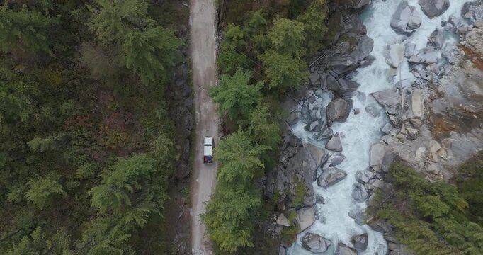 Annapurna Circuit, Manang, Nepal, aerial tracking shot of a 4x4 off-road jeep driving on a dirt road beside the rushing Marsyangdi River on the cliff side.