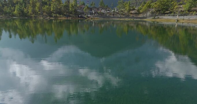 Annapurna Circuit, Manang, Nepal, aerial reveal shot rising over the pristine Green Lake around a pine forest to reveal the mountain scene in the background