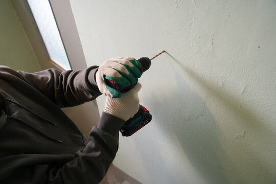Builder hands drilling wall with cordless drill driver