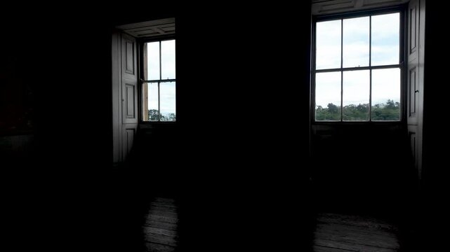 Sunlight beams moving across the wooden floor of a dark and empty room with two large windows