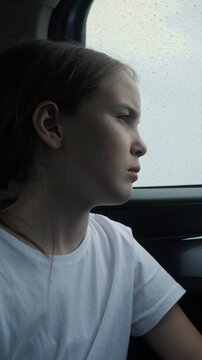 Unhappy and lonely young girl with a thoughtful expression looking out the car window during a downpour, feeling melancholic and pensive while traveling on a gloomy autumn day