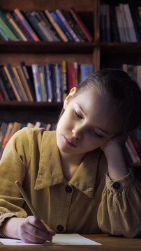 Sleepy and tired young schoolgirl falling asleep while doing her homework late at night, a smart kid yawning and writing a letter or studying for an exam in the library