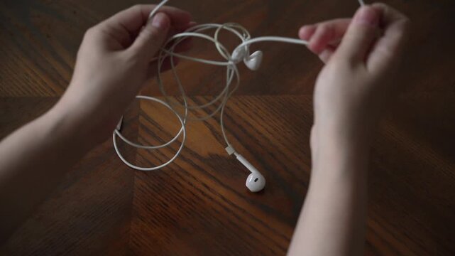 Hands are struggling to untangle a pair of earphones with intertwined cables, showcasing the common hassle of tangled wire.	