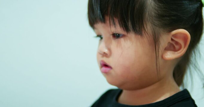 Young Asian toddler interacts with a digital tablet indoors. She watches an educational video, illustrating early learning, childhood curiosity, and everyday life with technology.