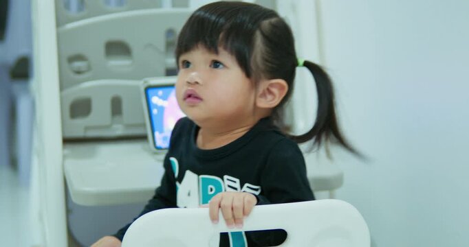 A curious toddler girl is engaged with an educational video on a tablet. This authentic home scene highlights early childhood development, screen time, and digital native generation.