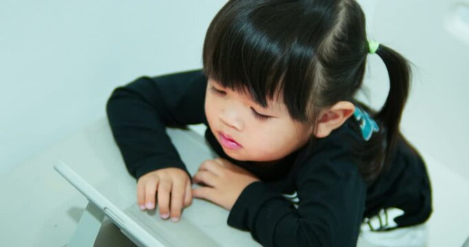 A curious toddler girl is engaged with an educational video on a tablet. This authentic home scene highlights early childhood development, screen time, and digital native generation.