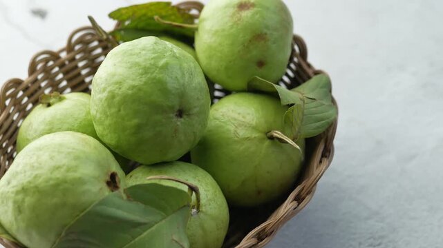 Fresh green guavas with leaves presented in brown wicker basket, rotating on white background, cinematic studio shot, organic fruit for healthy diet