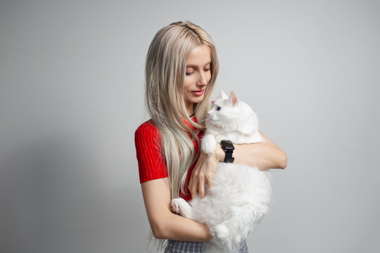 Young blonde girl with fluffy white cat in hands isolated on grey background. Studio portrait.