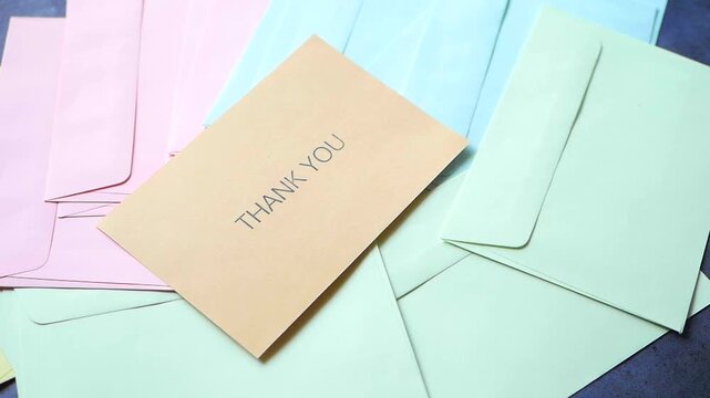 Person picking up brown thank you card from pile of colorful envelopes on table
