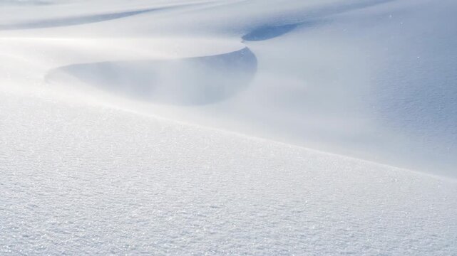 Close-up view of pristine white snow surface texture creating natural abstract winter background with smooth shapes and deep blue shade.
