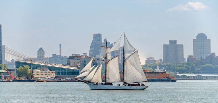 Schooner under full sail on East River near Brooklyn Bridge, New York. Vessel with two masts, white sails, East River, Brooklyn skyline, Brooklyn Bridge visible, daytime