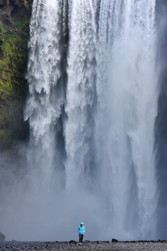 Hiker standing before the immense Skogafoss waterfall, Iceland
