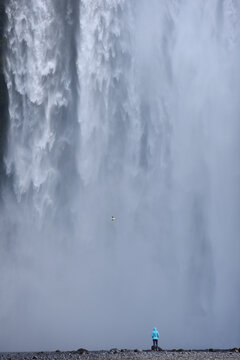 A hiker standing below the towering Skogafoss waterfall, Iceland