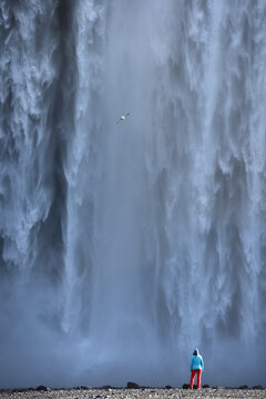A hiker standing below the towering Skogafoss waterfall, Iceland