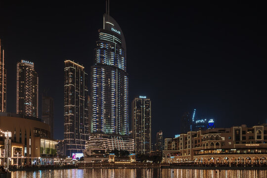 A night view of the illuminated fountains at Dubai Fountain Lake with the EMAAR building and skyscrapers in the background in Dubai mall, United Arab Emirates.