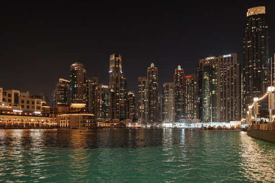 A night view of the illuminated fountains at Dubai Fountain Lake with the EMAAR building and skyscrapers in the background in Dubai mall, United Arab Emirates.