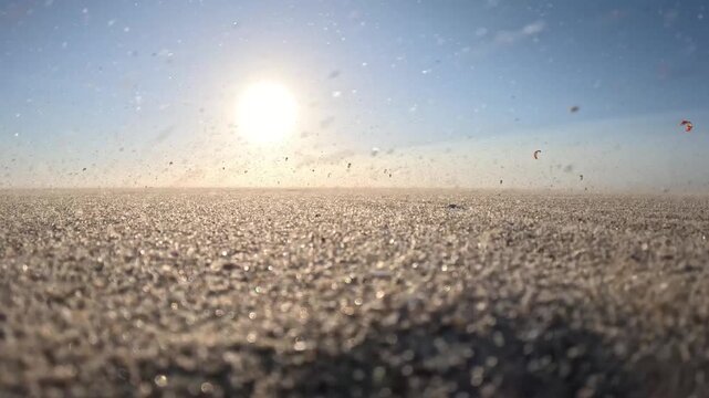 Scenic sunset on Kijkduin Beach with airborne sand and kitesurfers riding the North Sea in the distance
