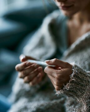 Woman holding a home pregnancy test with anxious anticipation at home. Concept of fertility journey, infertility, trying to conceive, uncertainty, reproductive health and emotional stress