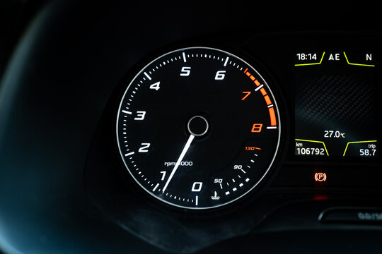 Close up of a car dashboard instrument cluster featuring a illuminated tachometer gauge and engine temperature scale.