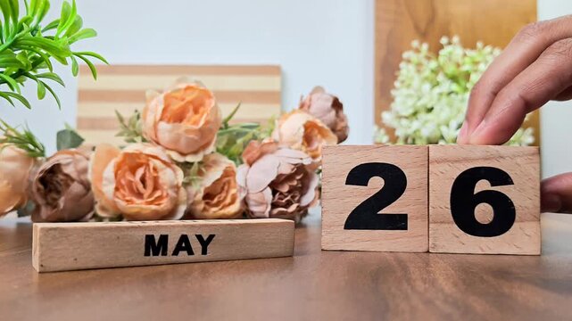 Hand placing wooden calendar blocks showing may 26 on a wooden table