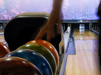 Fototapeta premium Person picking up a bowling ball from the ball return in an indoor bowling center. Horizontal format