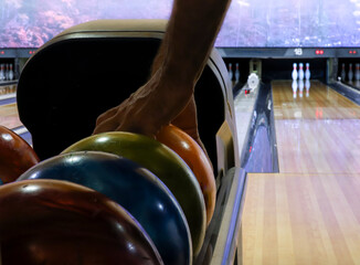 Fototapeta premium Person picking up a bowling ball from the ball return in an indoor bowling center. Horizontal format