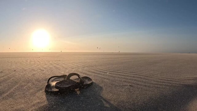 Cinematic flip-flops on Kijkduin Beach during a sunset sandstorm with distant kitesurfers on the North Sea