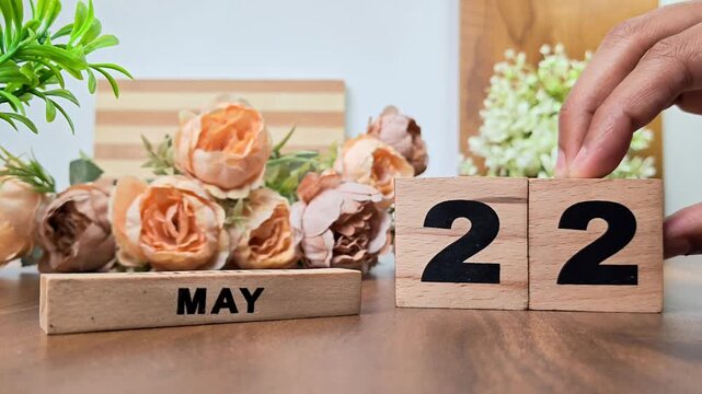 Hand placing wooden calendar blocks showing may 22 on a wooden table