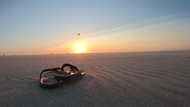 Atmospheric sunset on the Dutch coast with flip-flops in the sand and kitesurfers on the horizon