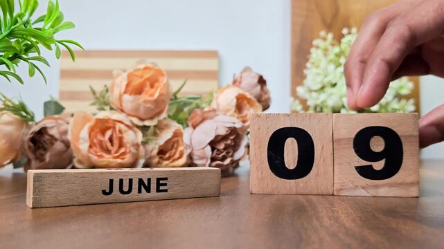 Hand placing wooden calendar blocks showing june 9 on a wooden table