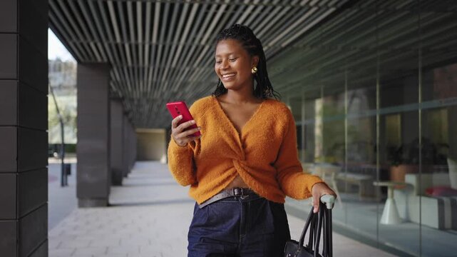 Stylish African American woman using red and orange smartphone app in the city