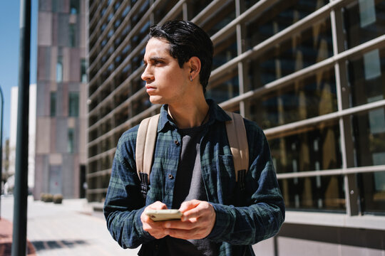 Young hispanic man using mobile phone in modern urban city. Happy university student smiling at campus