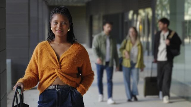 Portrait of stylish African American traveler woman standing with suitcase in hotel airport lobby