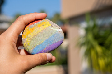 Close-up of a hand holding a hand painted rainbow stone against a clear blue sky. Concept of hope, happiness, creativity and positive emotions © leroy
