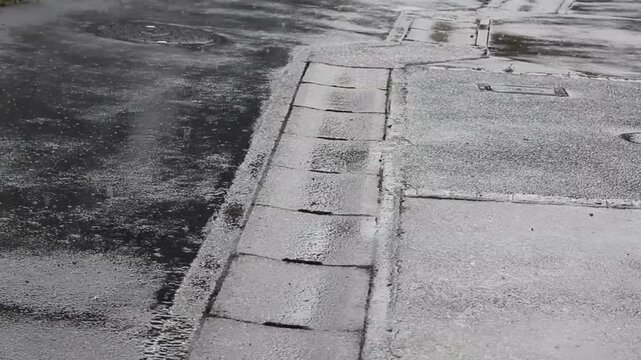 Rainwater flowing along urban street curb into storm drain during heavy rainfall in local Japanese urban area
