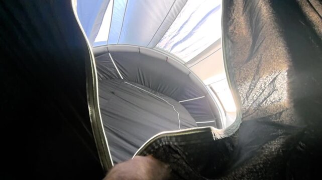 Inside the cozy confines of a tent, a man eagerly pulls back the fabric, unveiling the sunlight and fresh air beyond. The moment is filled with curiosity and excitement.