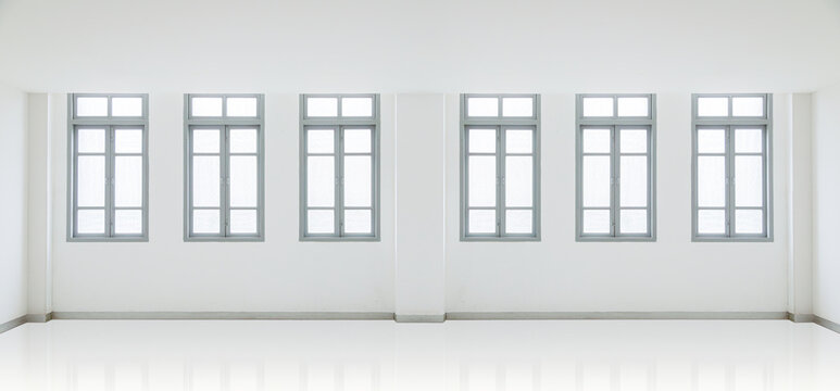 A clean, symmetrical, and minimalist interior of an empty white room featuring a row of classic grey-framed windows and a reflective white floor, ideal for architectural backgrounds.