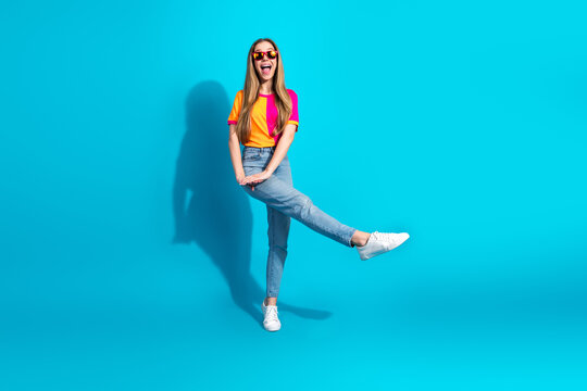 Young stylish woman in a bright color block top jumps against a blue background for a fun fashion shot