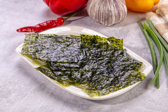Crispy seaweed snack sheets on plate with fresh vegetables and spices