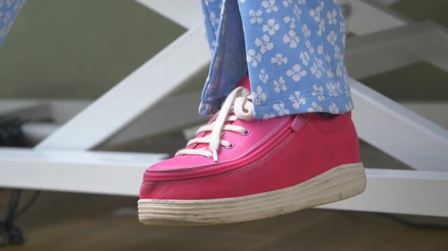 Close up of person wearing bright pink adaptive zipper shoes sitting on white medical table with blue floral pants