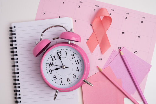 Pink ribbon and alarm clock on a calendar for breast cancer awareness and pink october concept
